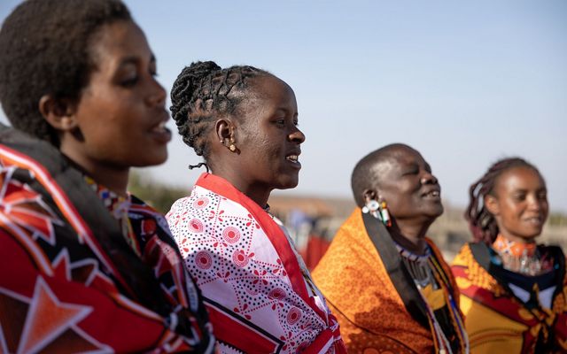 A group of women stand outside in a row and smile to celebrate the introduction of her son to her family and friends.