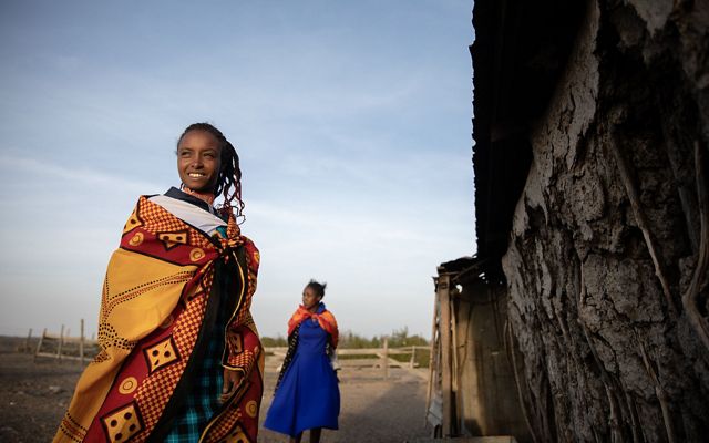 A woman smiling next to her home.