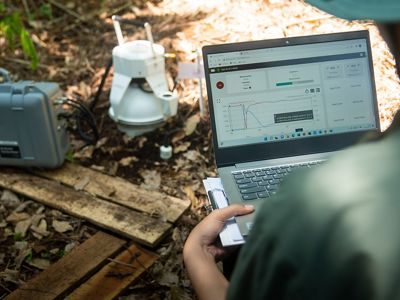 A person holds a laptop on their lap to measure the benefits of peatlands.